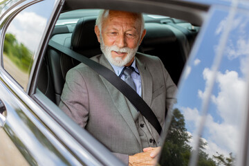Senior gentleman in a sharp suit smiling while buckled up in his car