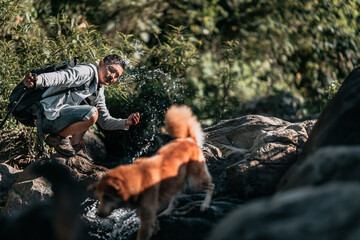 A hiker is enjoying water from a stream with his dog during a hike..