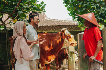 Young Asian Muslim couple doing negotiation with the cattleman buying livestock cows for sacrifices. Eid Al Adha concept. - Powered by Adobe