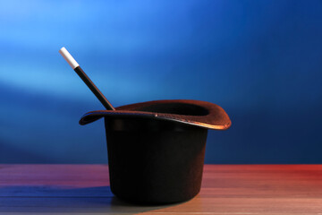 Magician's hat and wand on wooden table against blue background