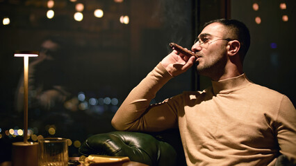 Businessman smokes cigar in restaurant. Media. Man smokes cigar in luxury restaurant at night....