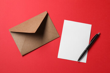 Blank sheet of paper, letter envelope and pen on red background, top view. Space for text