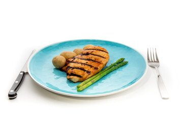 grilled chicken breast with asparagus in a on a blue plate with a knife and fork isolated on white