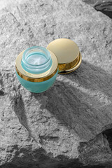 An elegant cosmetic product with a gold cap stands on a gray stone background with light effects. Concept of a premium expensive brand and skin and face care for women