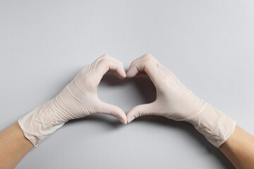 Doctor wearing white medical gloves making heart gesture on grey background, top view