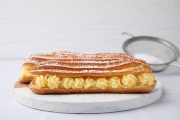 Delicious eclairs filled with cream on white table
