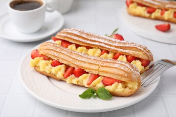 Delicious eclairs filled with cream, strawberries and mint on white tiled table