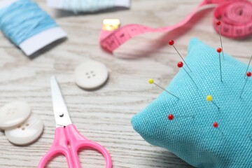 Light blue pincushion with pins and other sewing tools on wooden table, closeup