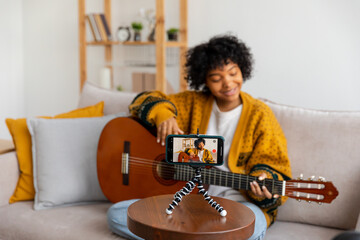 Blogger guitarist. African american girl blogger playing guitar talking to webcam recording vlog. Social media influencer woman streaming at home indoors. Music content creator broadcast tutorial