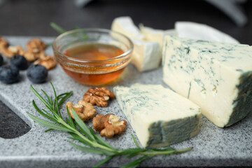 Close-up of cheese plate served with honey, blueberries and hazel nuts on stone cutting board