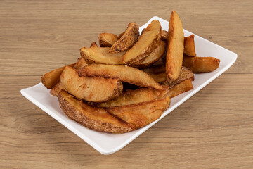 A white square plate of deep fried potato wedges on a wooden table