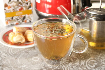 Herbal tea in glass cup. Teapot on table, vanilla eclair pie In kitchen.