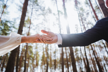 Happy bride and groom holding hands in forest, surrounded by trees and grass