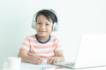 A little boy is smiling while using the computer laptop with headphones