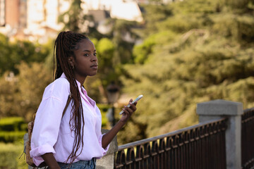 Side view of a thoughtful african american woman standing and holding a smartphone