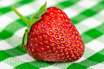 Large red strawberry on a background of a green tablecloth