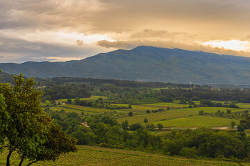 2024-05-14 LUSH COUNTRY SIDE IN THE BEDOIN AREA OF PROVENCE FRANCE WITH A VIEW OF A GREEN VALLEY AND CLOUD COVERED MOUNT VONTOUX