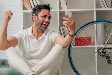 attractive man at home with mobile phone celebrating euphoric