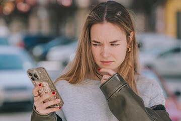 girl looking with thoughtful suspicion at the mobile phone on the street