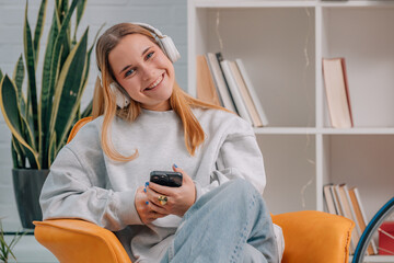 young woman sitting on the sofa at home with headphones and mobile phone