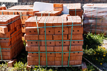 A pallet of neatly stacked red clay bricks wrapped in plastic is ready for use on a sunny day at a...