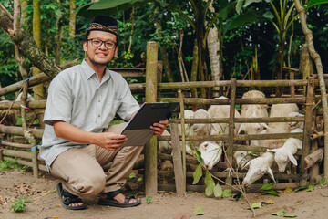 Smiling Asian Muslim man kneeling down holding a document with the livestock goats for sacrifices...