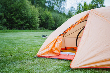 Experience the tranquility of camping in a meadow with an orange tent, surrounded by lush greenery,...
