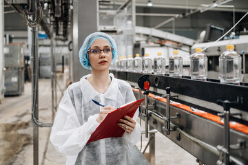 Female worker in protective workwear working in medical supplies research and production factory and checking canisters of distilled water before shipment. Inspection quality control.