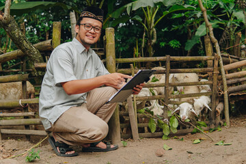Excited young Asian Muslim man pointing to document he holds with livestock goats for sacrifices...