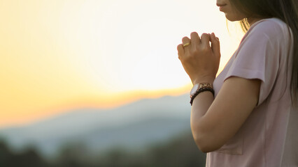 young woman clasped her hands together in prayer asking for forgiveness from God based on her...