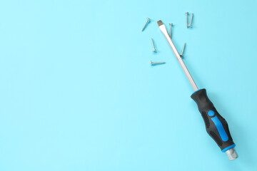 Screwdriver with black handle and screws on light blue background, flat lay. Space for text
