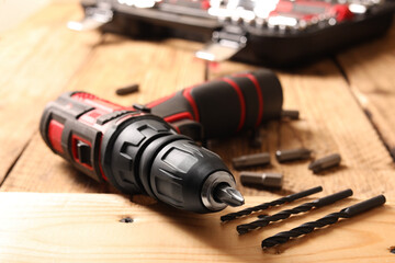 Electric screwdriver with bits and drills on wooden table, closeup