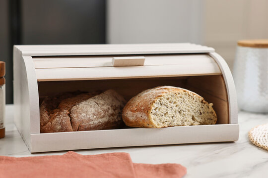 Wooden bread basket with freshly baked loaves on white marble table in kitchen