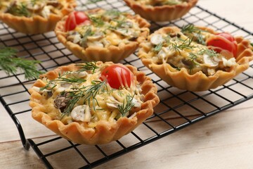 Tasty tartlets with cheese, tomatoes, mushrooms and dill on wooden table, closeup