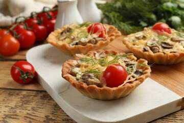 Tasty tartlets with cheese, tomatoes and dill on wooden table, closeup