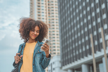 Happy young African American woman using social media on mobile phone on street in a urban city....