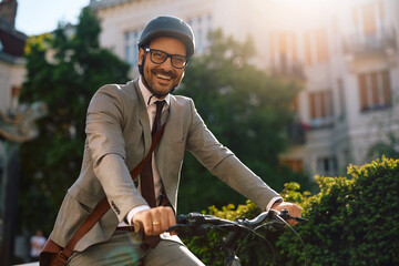 Happy businessman riding bicycle in city and looking at camera.