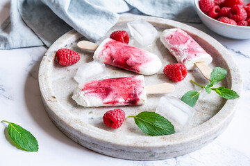 Homemade raspberry popsicles on tray with ice and berries