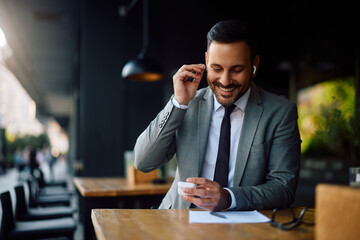 Happy businessman using earbuds while sitting in café.