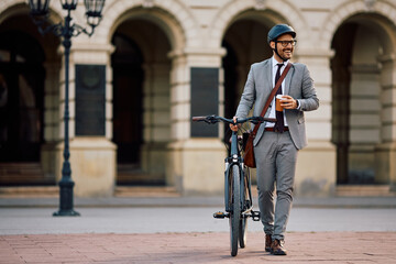 Happy businessman with coffee to go and bicycle walking on city street.