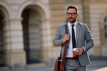 Mid adult businessman with takeaway coffee walking on city street.