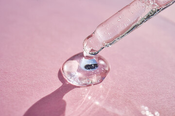 Pipette with serum shimmering in the sun on a pink background.