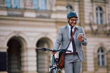 Happy businessman text messaging on mobile phone while pushing bicycle on street.