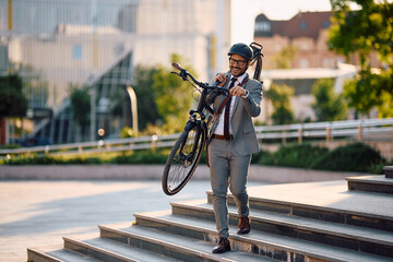 Happy businessman carrying his bike on his shoulder in city and looking at camera.