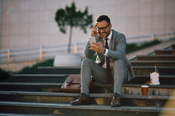 Happy businessman reading text message on cell phone in city.