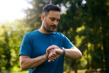 Male athlete checking heart rate on smart watch while working out  in nature.