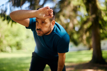Exhausted athletic man taking  break after running in nature.