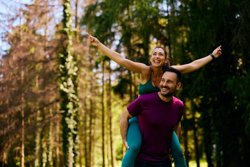 Fototapeta premium Happy couple having fun while piggybacking during sports training in nature.