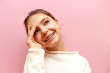modest pensive teenage girl with braces thinks and imagines on a pink isolated background, the...