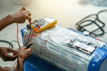 Electrician hands using a multimeter to check the voltage of the electrical system in lithium...